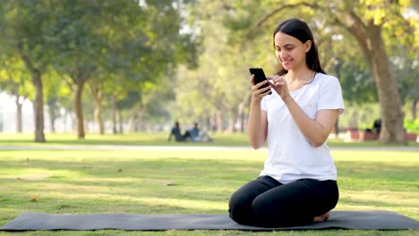 indian yoga girl scrolling through phone in a park in morning