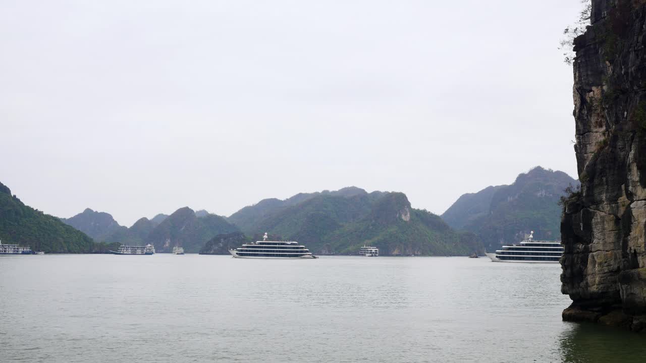 Several luxury cruise ships gracefully navigate through the emerald waters of Ha Long Bay, surrounded by towering limestone karsts and misty mountains in the ethereal Vietnamese seascape