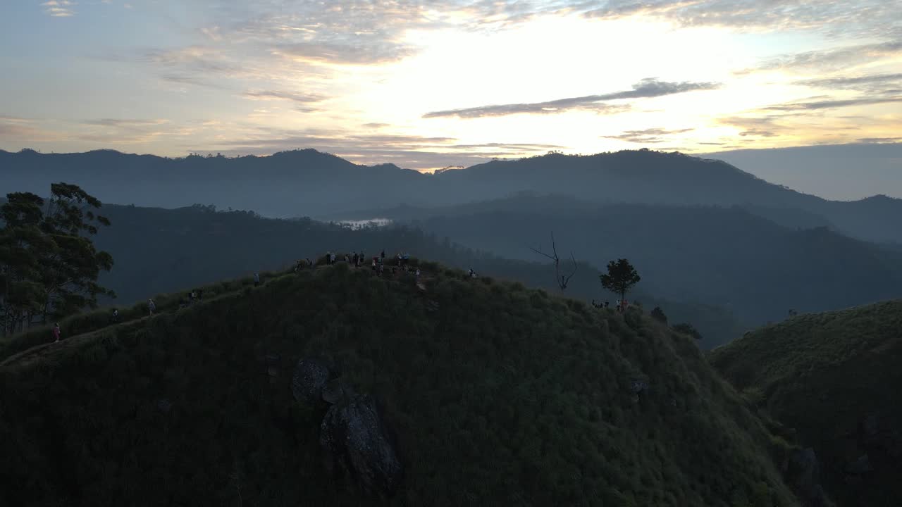 Rekaman drone udara wisatawan berjalan di sepanjang lereng hijau menuju Puncak Little Adam di Sri Lanka pada pagi hari.