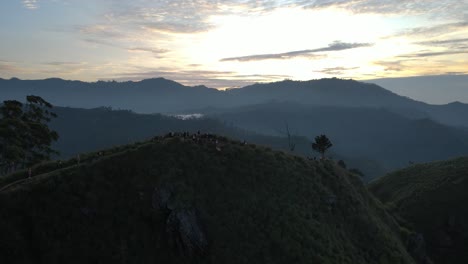 Aerial-drone-shot-of-tourists-walking-along-green-slopes-leading-to-little-Adam-peak-in-Sri-Lanka-during-morning-time