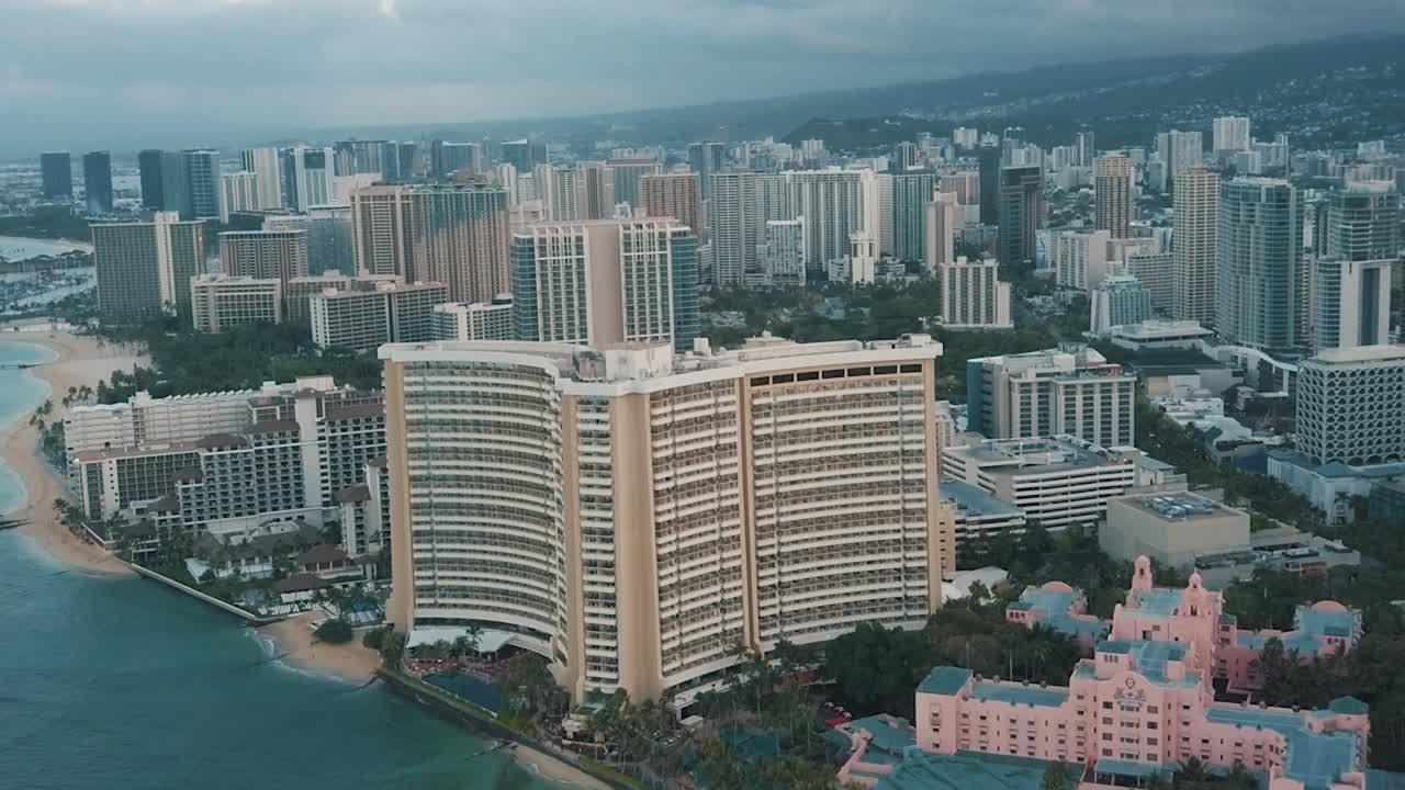 Panning aerial drone slowly flying over a colorful Honolulu Skyline while Sunset in Oahu, Hawaii with Waikiki Beach as a special point of interest.