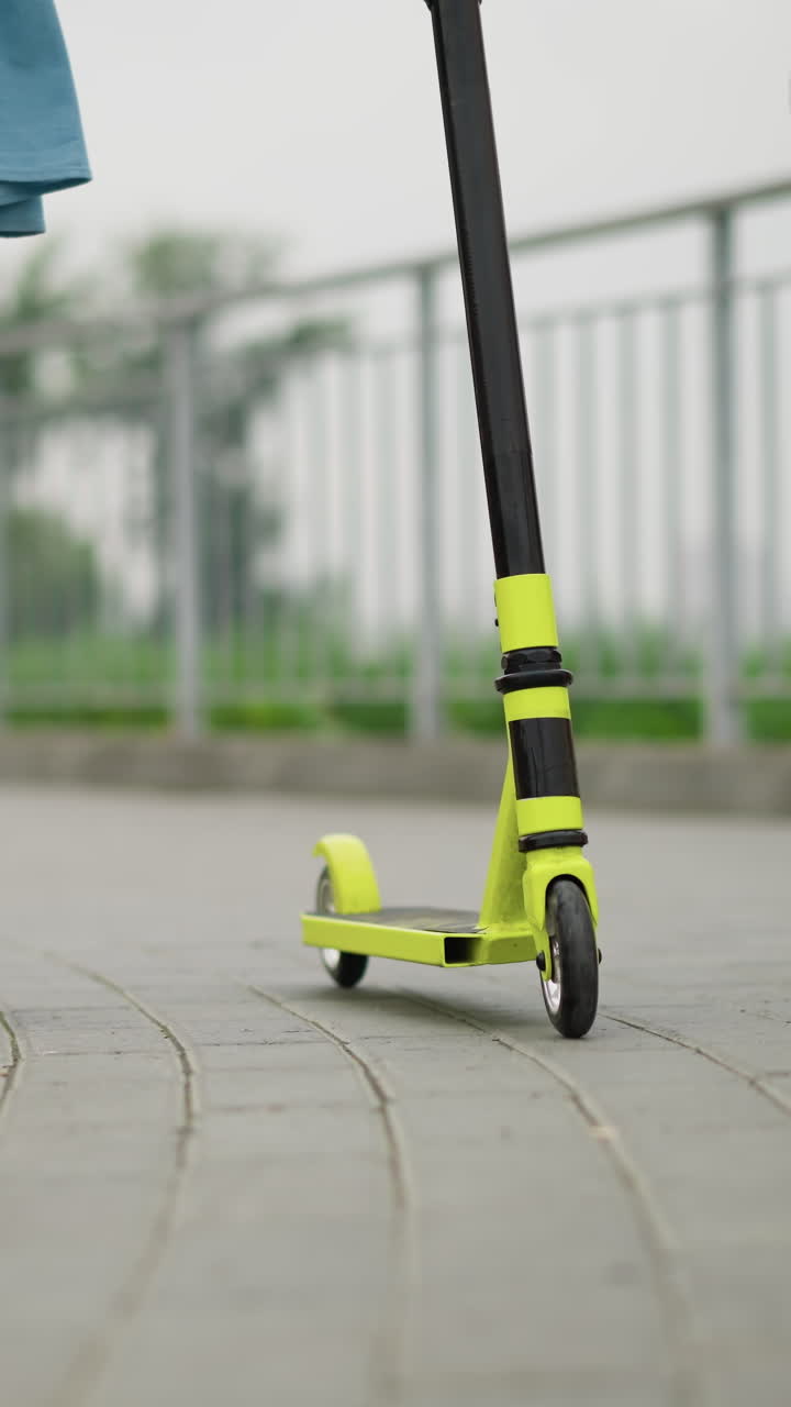 여인과 아이가 포장된 보행로를 걸어서 노란 스쿠터를 밀고 있는 아래의 모습, 둘 다 다리와 스쿠터에 초점을 맞추며 캐주얼하게 옷을 입고 있다.