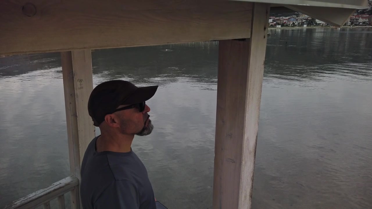 High angle shot of lifeguard with cap and sunglasses monitoring sea from wooden watchtower. Concept for beach safety, coastal surveillance, rescue patrol, and protection.
