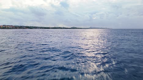 Sunlight-breaks-between-cloudy-skys-shimmering-on-deep-blue-ocean-water-with-Caribbean-tropical-paradise-coastline-on-horizon