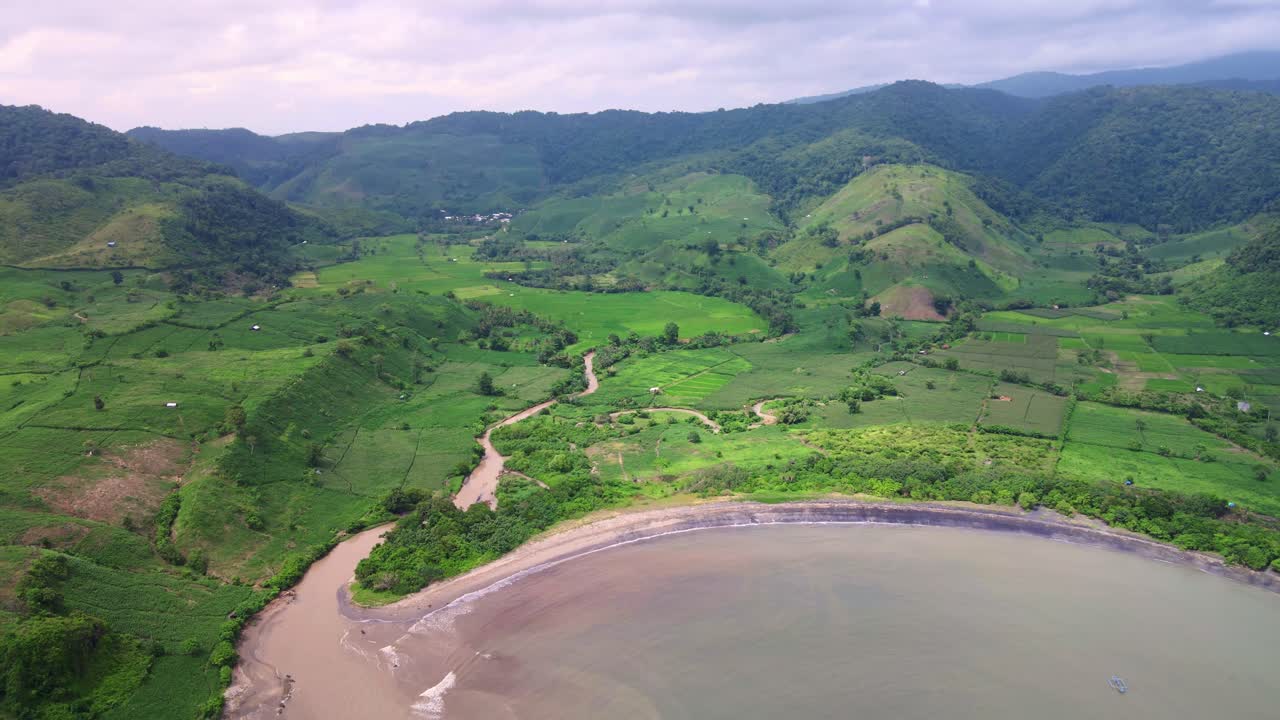toma épica de drones de una playa escondida frente al océano con campos agrícolas de arroz con fondo de montaña en la isla de sumbawa, indonesia
