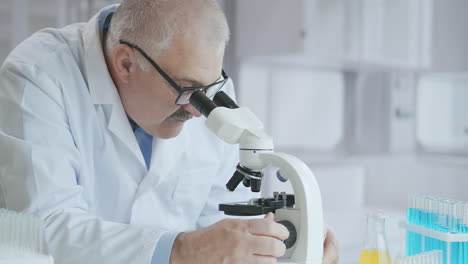 bearded caucasian male researcher wearing protective glasses and working with a microscope spbas. scientist using microscope in a laboratory. search for coronavirus vaccine. high quality 4k footage