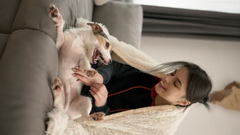 smiling woman sitting on couch in blanket with her small dog jack russell terrier