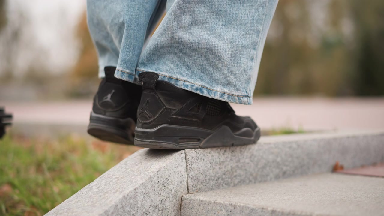 Close up of person lower legs and feet wearing light blue jeans as they step down from gray stone steps. black sneakers with visible texture interact naturally showing movement