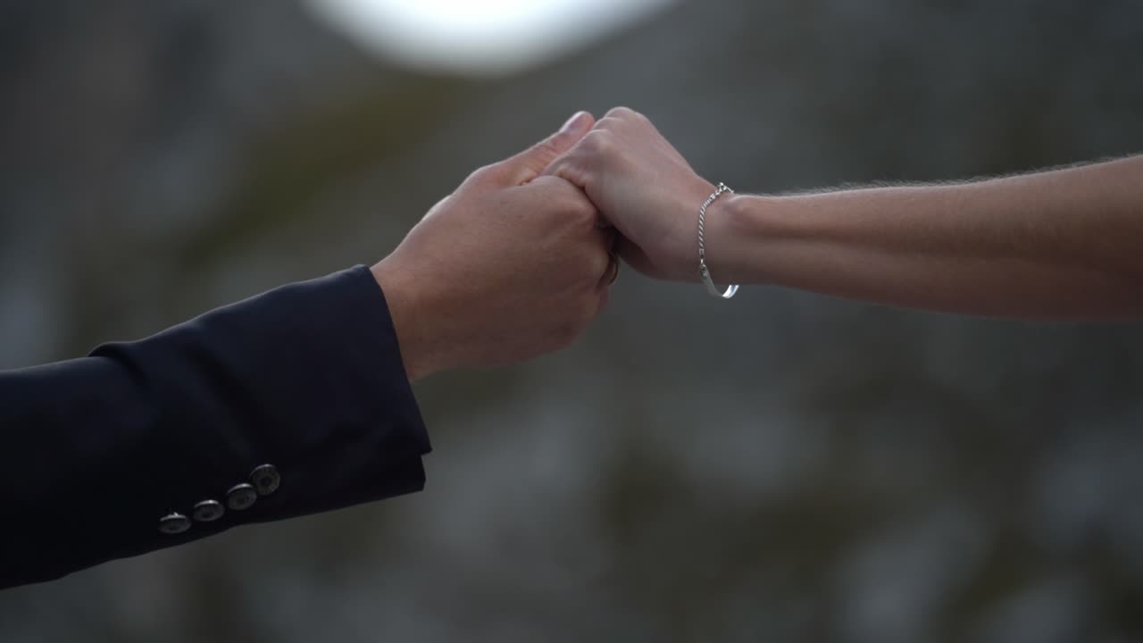 Male and female hand reaching each other holding gently and slowly leaving again - suit and bracelet