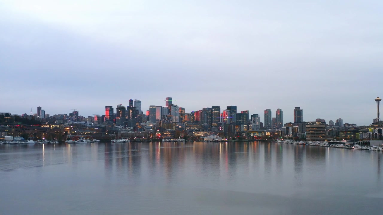 Vista aerea con drone sul tranquillo Lago Union che riflette gli edifici del centro di Seattle e lo Space Needle. Luci calde brillano lungo il lungomare sotto un cielo serale velato