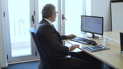 serious busy mature investor sitting and working at monitor