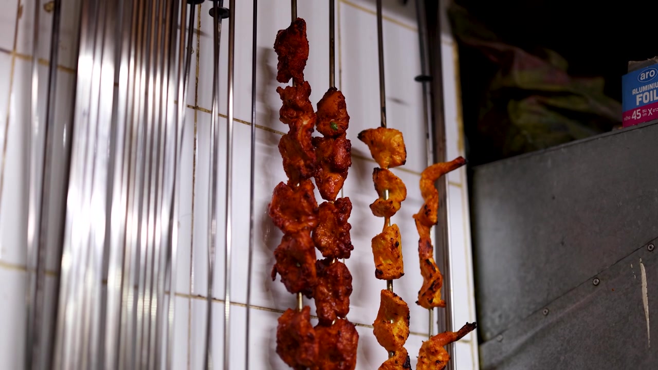 Primo piano di carne marinata su spiedini di metallo appesi a una bancarella di street food.