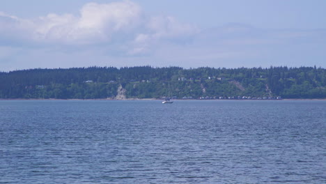 Distant-sailboat-motoring-past-beach-at-Camano-Island-State-Park,-Washington-State-10sec-24fps-slow-motion