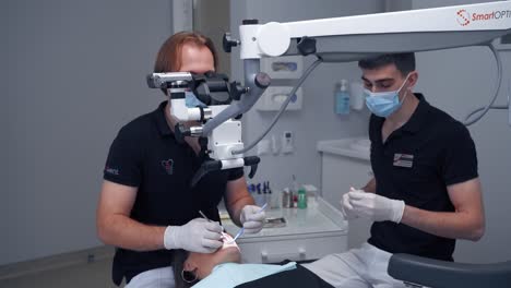 man dentist uses contemporary equipment. professional doctor treating patient's teeth through the microscope in dental office. specialist and his assistant in clinic.