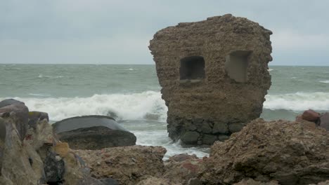 grandes olas tormentosas rompiendo contra las ruinas abandonadas del edificio de fortificación junto al mar en los fuertes del norte de karosta en liepaja, costa del mar báltico, salpicadura de olas, día nublado, plano medio