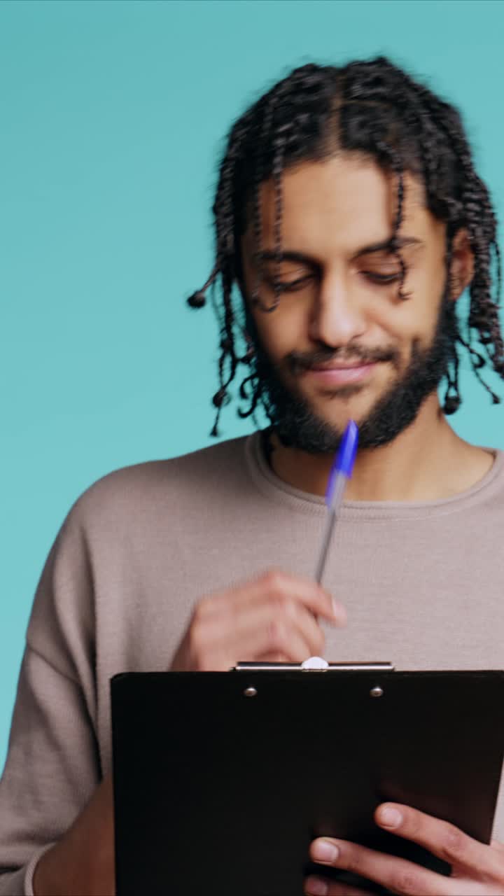 Video verticale. Uomo creativo che pensa a nuove idee, scrive su carta usando una penna, sfondo da studio