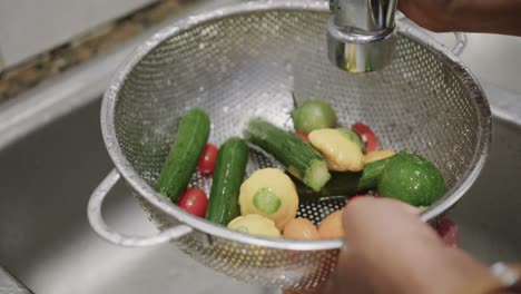 Hands-of-biracial-woman-washing-colander-of-vegetables-in-kitchen-sink,-slow-motion