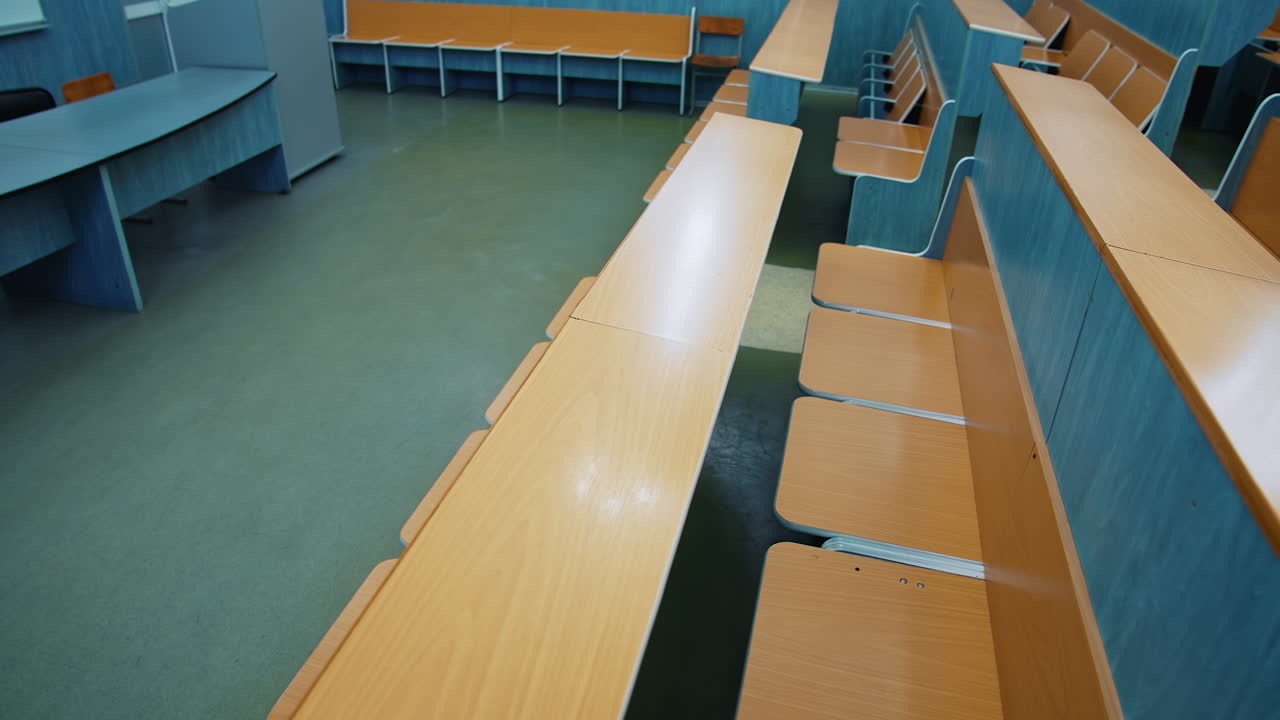 Empty auditorium for students. Rows of wooden tables and chairs in the university. Nobody in the class during pandemic.
