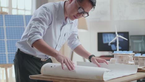 asian man looking at the blueprint with model small house with solar panel