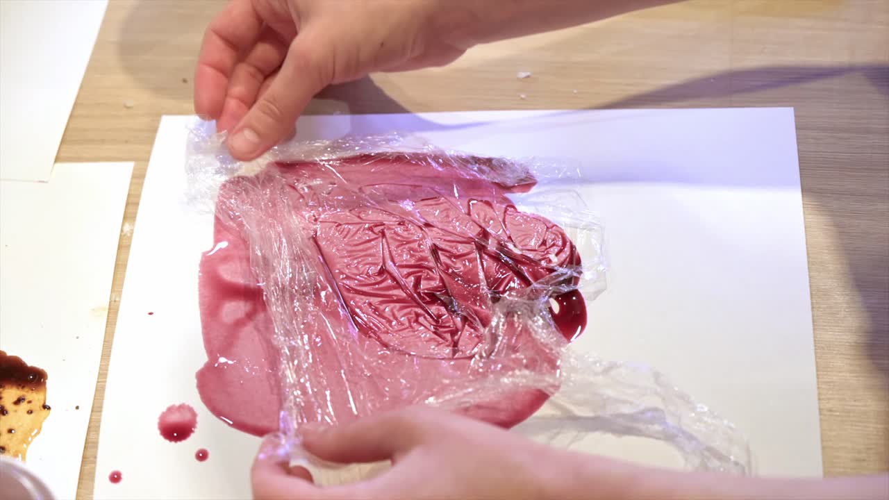 A woman in a studio painting on paper with red wine and cellophane, close view, slow motion