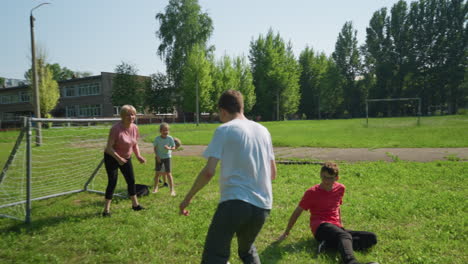 family enjoys a lively outdoor soccer game as the son in white dribbles the ball past his sliding brother and scores into the goalpost, with their mother watching the ball enter the net