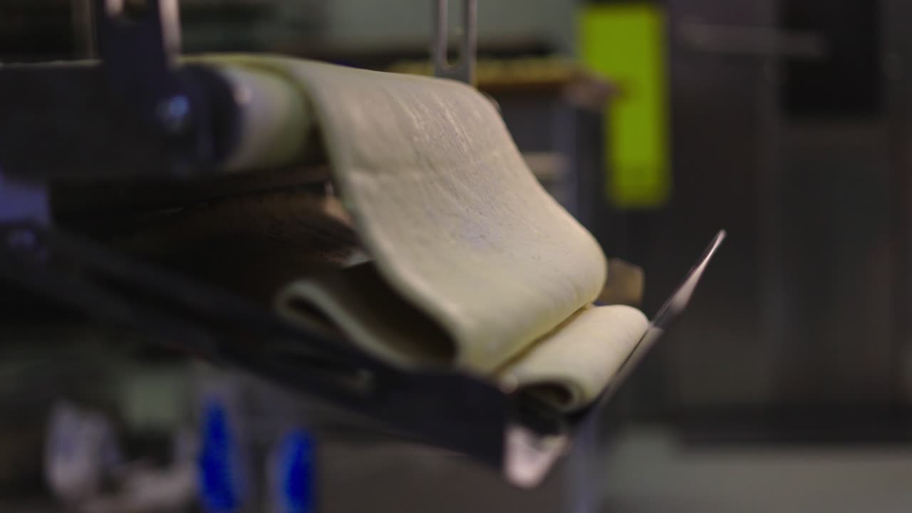 대형 도우 볼이 디저트 가공을 위해 준비된 페이스트리 기계의 컨베이어를 나갑니다.