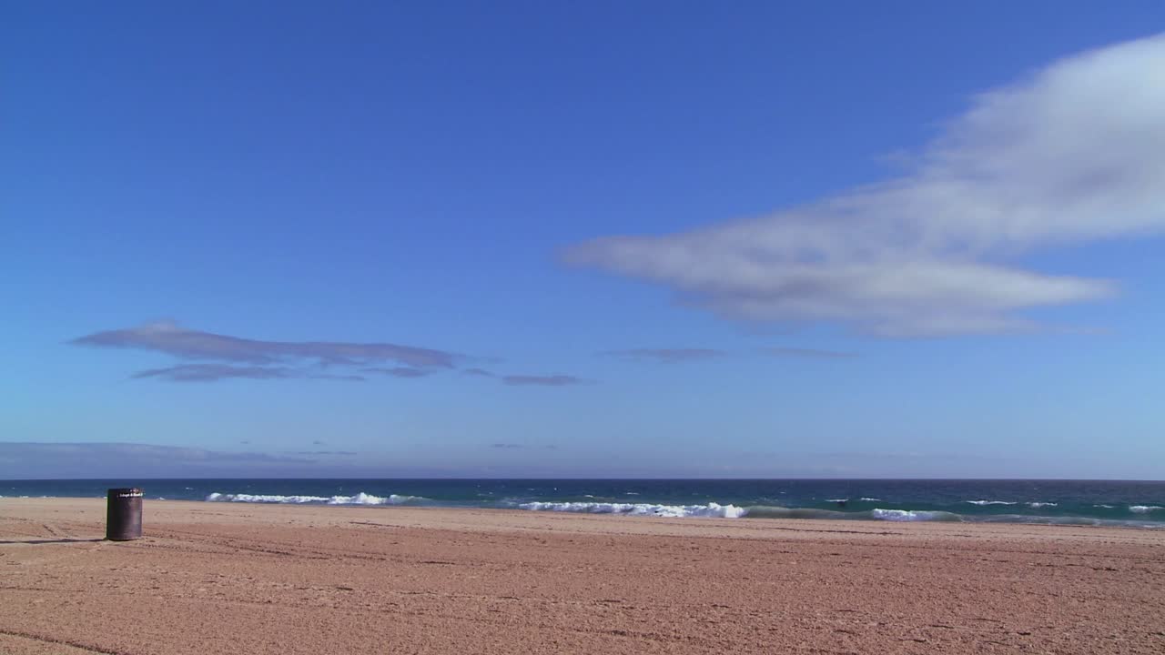 una playa vacía con un bote de basura solitario y un cielo azul