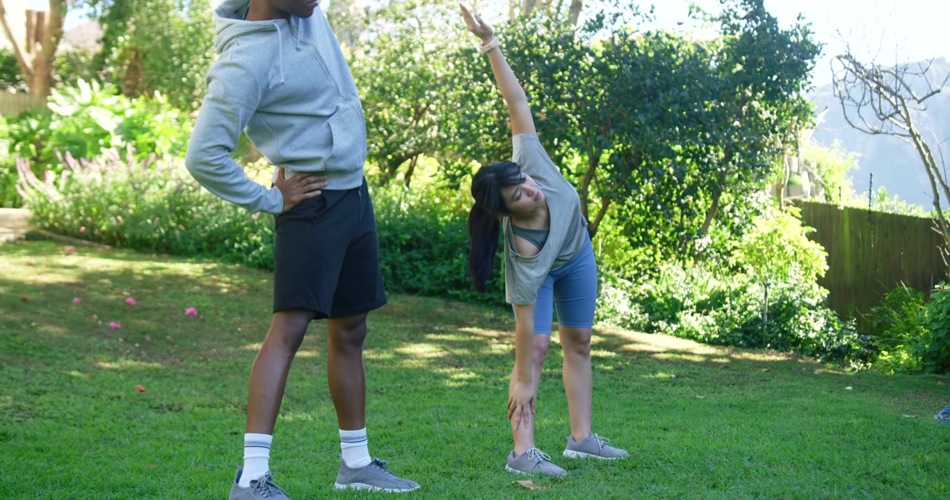 Diversos compañeros de entrenamiento calentando después de la señal, estirándose lateralmente en un césped verde con zapatillas grises.