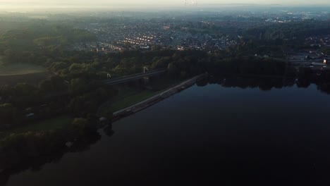 descending aerial forward moving over lake reservoir towards rail bridge