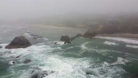 4k 30fps aerial footage oregon coast - calm foggy overcast morning - static shot high amongst clouds, waves crashing against mossy stone rocky pacific ocean shore - dji drone video