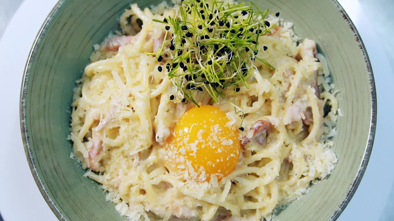 Tasty restaurant dish. Cooked meal ready to eat. Delicious italian food in plate is spinning. Pasta with cheese and raw yolk decorated with sprouts. Close-up. Top view