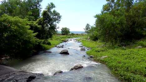 small-clear-flowing-water-from-river-cutting-its-way-through-big-rocks-and-lush-green-countryside-to-the-Pacific-ocean-under-blue-sky-and-white-clouds