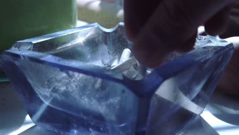 Close-up-of-a-hand-with-a-cigarette-knocking-the-ash-off-and-then-tipping-the-cigarette-into-the-ashtray