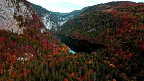 drone approaching an isolated mountaintop lake surrounded by leaves changing color