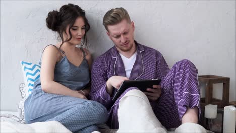 una pareja relajándose en la cama con una tableta.