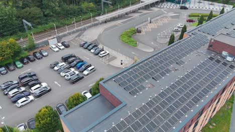 an aerial view of a building with solar panels on the roof, surrounded by a parking lot and greenery. the curved road and parked cars highlight the blend of urban infrastructure and sustainable design