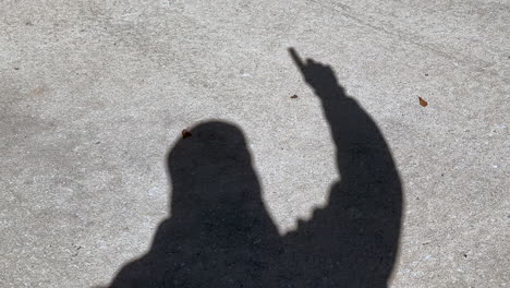 Shadow-of-man-waving-number-one-and-winner-sign-with-finger-on-hand,-concrete