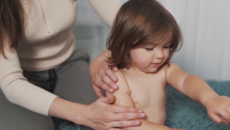las manos de mamá aplicando loción corporal a una linda niña de dos años en un pañal