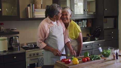 happy senior biracial couple wearing aprons preparing food in kitchen