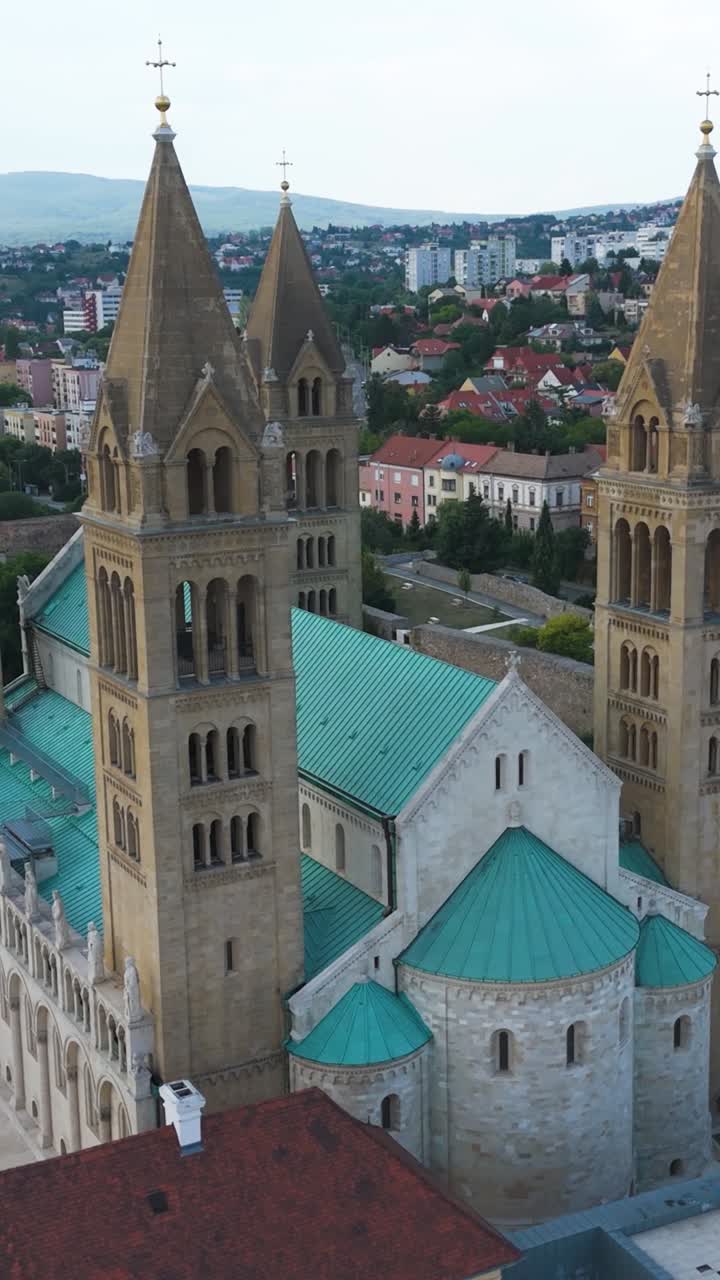 Luftfoto af Pécs-katedralen i lodret position, der fanger kuplen, tårnene og de urbane omgivelser