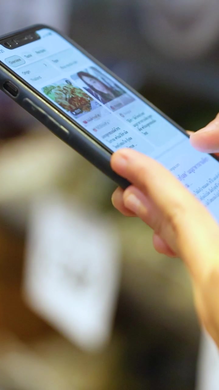 Hands holding a smartphone, browsing recipes in a well-lit cafe setting. Focus on screen interaction and casual atmosphere