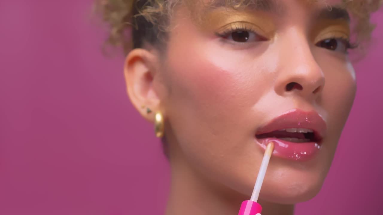 A sensual girl with beautiful face applies lip gloss to her pink lips