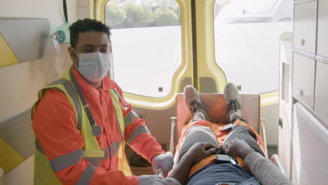 retrato de un paramédico masculino con mascarilla mirando la cámara mientras viaja en una ambulancia y cuida a un paciente estadounidense herido