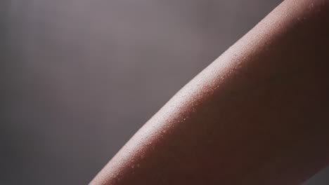 woman leg with water drops in bathroom closeup. bare lady leg covered with small droplets on light background. bathing procedures and spa at home