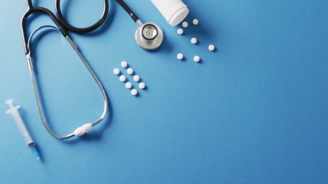 Video of stethoscope with syringe and white pills on blue background with copy space