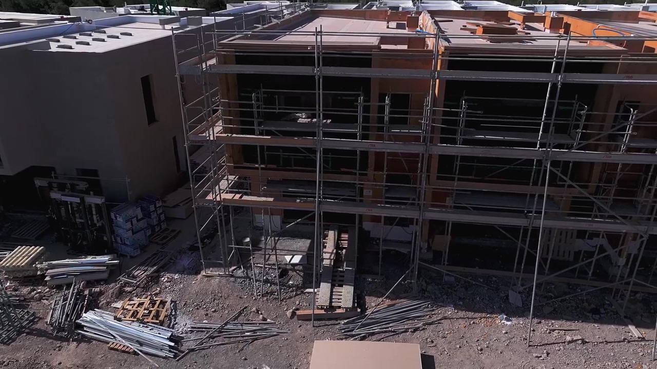 Drone view between modern residential buildings under construction, with extensive scaffolding, exposed structures and building materials showing an active urban development site