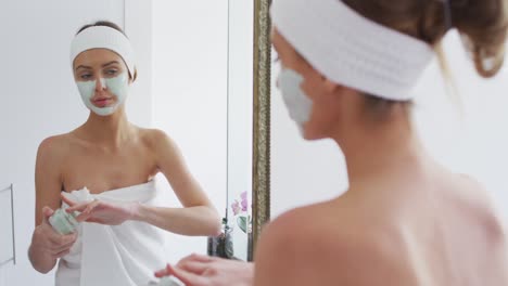 mujer aplicando una máscara facial mientras mira en el espejo en el baño