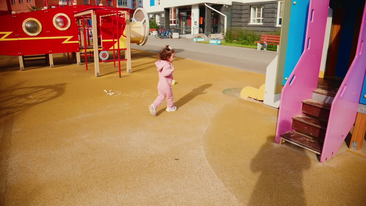 A Joyful Child in Pink Runs Through a Colorful Playground, Enjoying Playtime on a Sunny Day with Play Equipment and Bright Surroundings