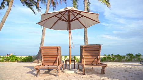 Dos-Asientos-Vacíos-De-Madera-Y-Una-Sombrilla-Bajo-Palmeras-En-Un-Destino-Tropical-Con-Vistas-Al-Mar-Y-Playa-De-Arena-Blanca