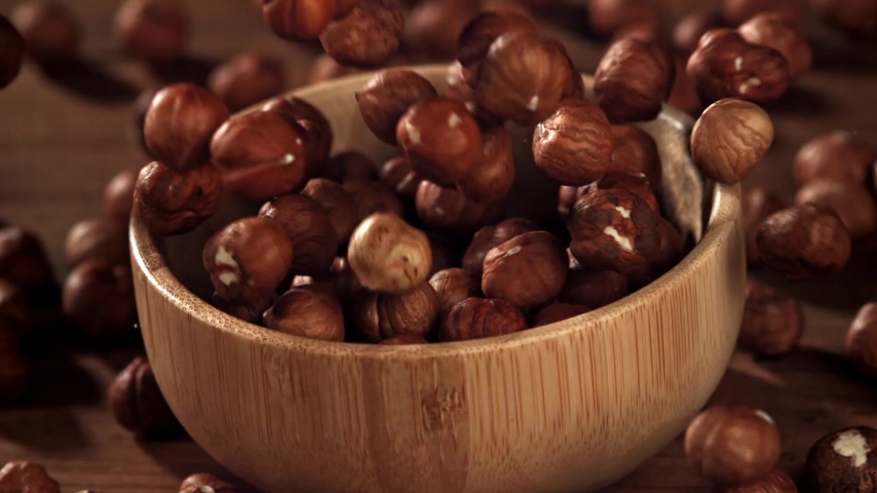 Nocciole sgusciate che cadono in una ciotola di legno al rallentatore